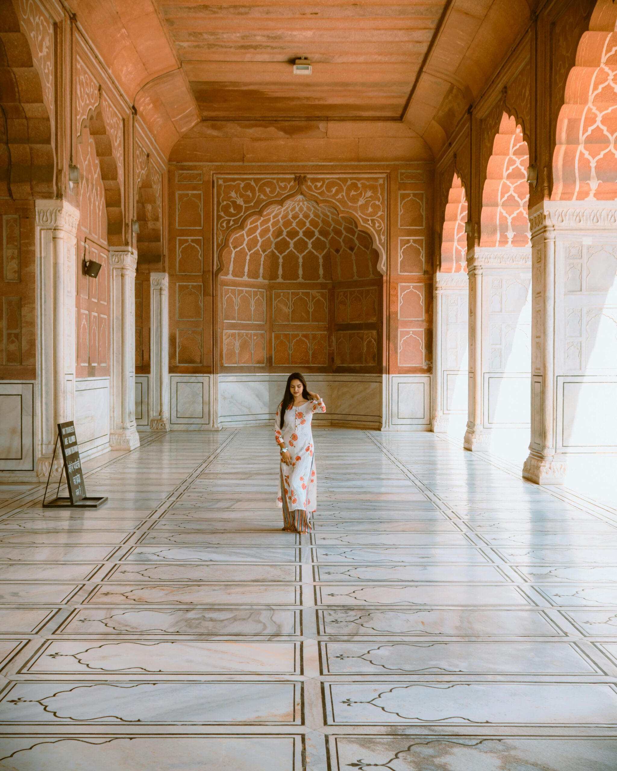 A woman stands in a sunlit marble hallway with traditional Indian architecture in New Delhi's palace.